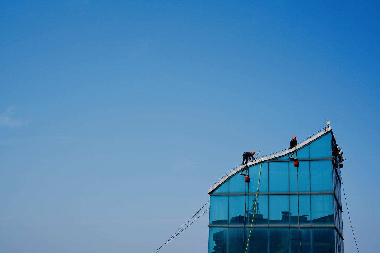 man in red shirt and black pants standing on blue building during daytime